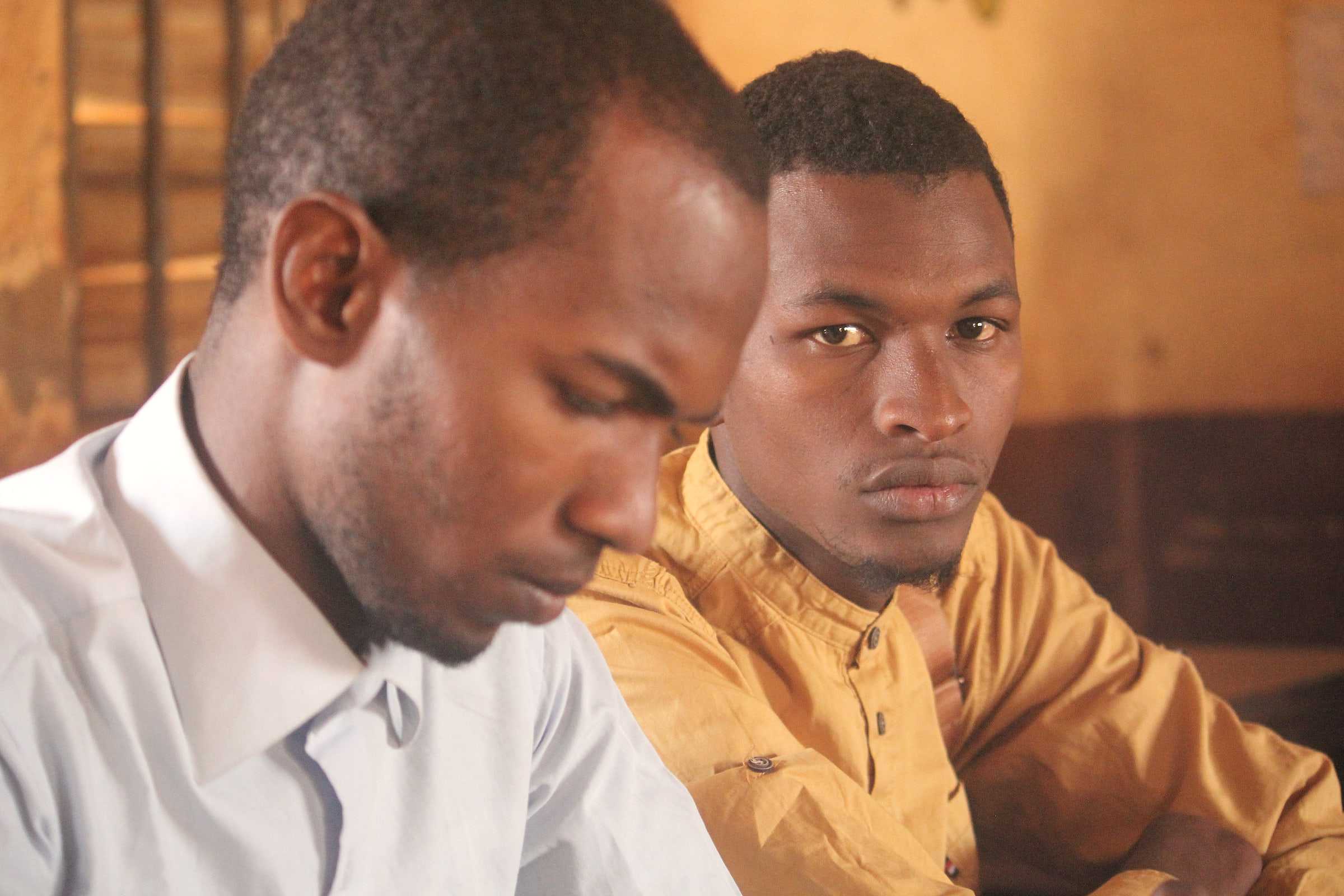Deux jeunes hommes attentifs, dans une lumière chaude, à Labé